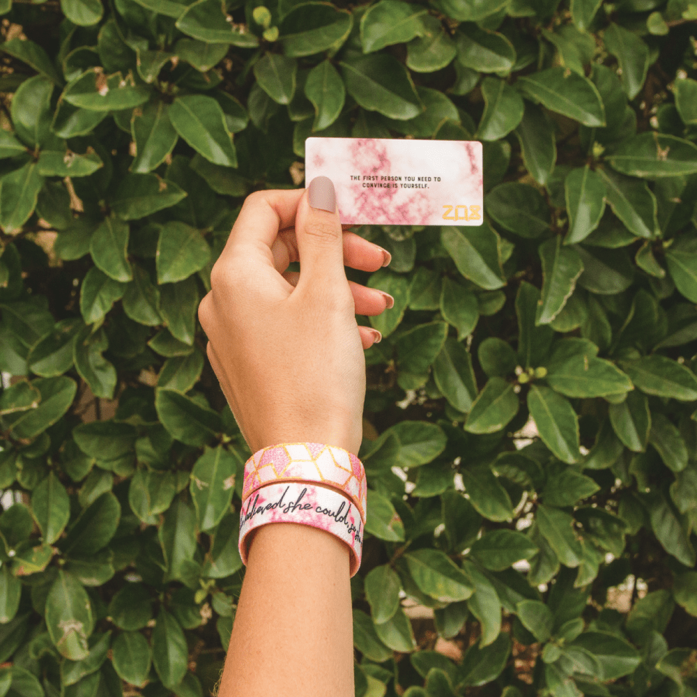 Lifestyle photo of someone holding the back of the card in front of a bush.