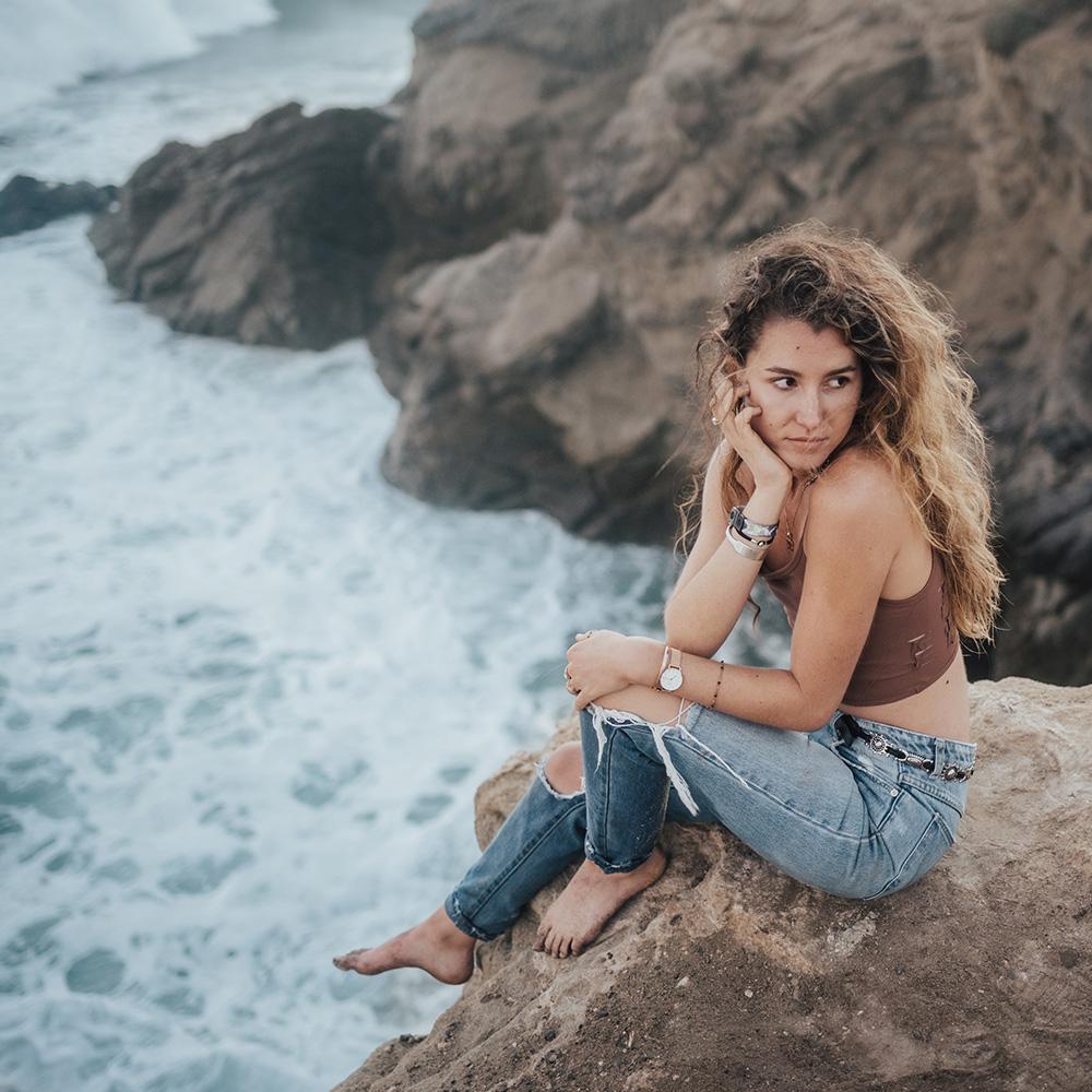 Lifestyle image of someone sitting on a rock over the ocean wearing dream on their wrist