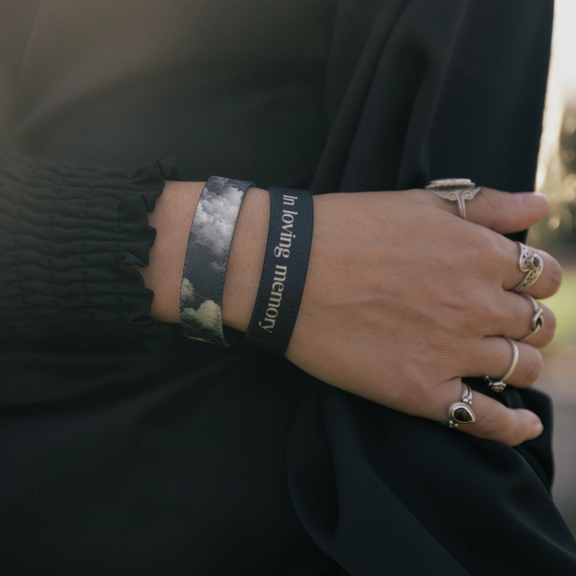 Close-up of a person wearing multiple bracelets and rings on a blurred natural background