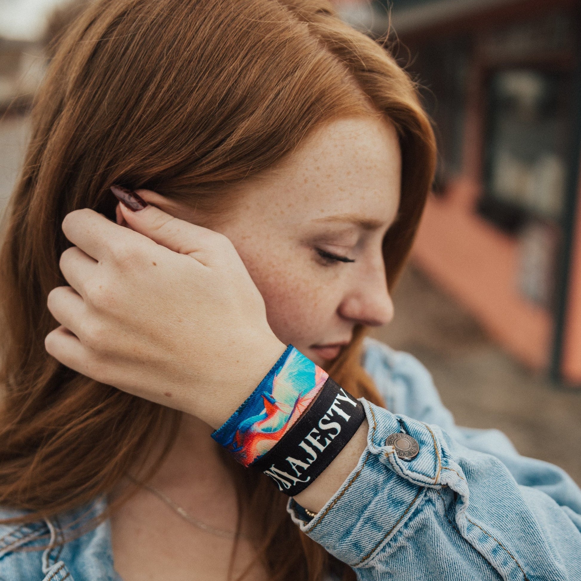 Person wearing a denim jacket and colorful bracelets with a blurred background