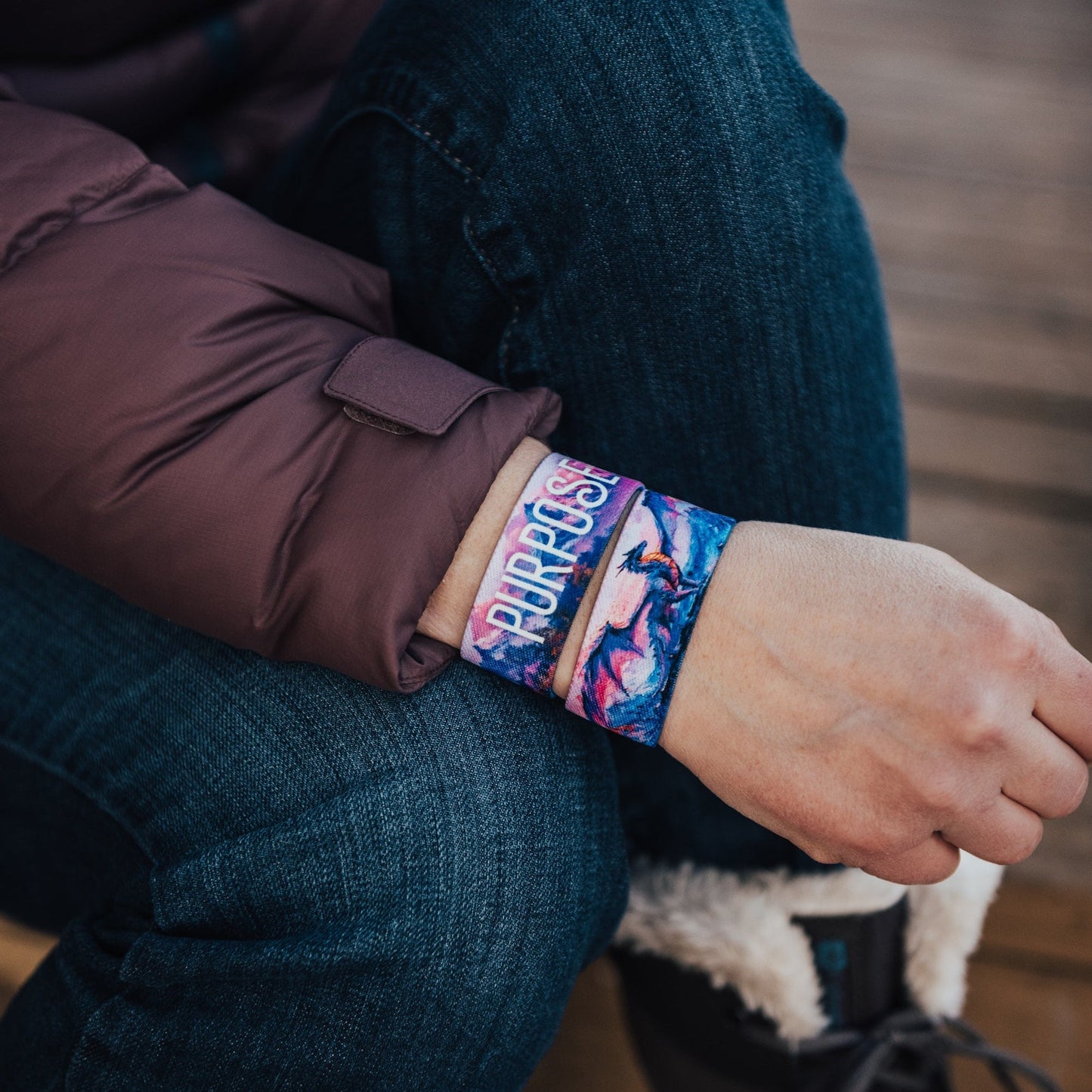 Person wearing a colorful wristband with text, sitting on a wooden floor.