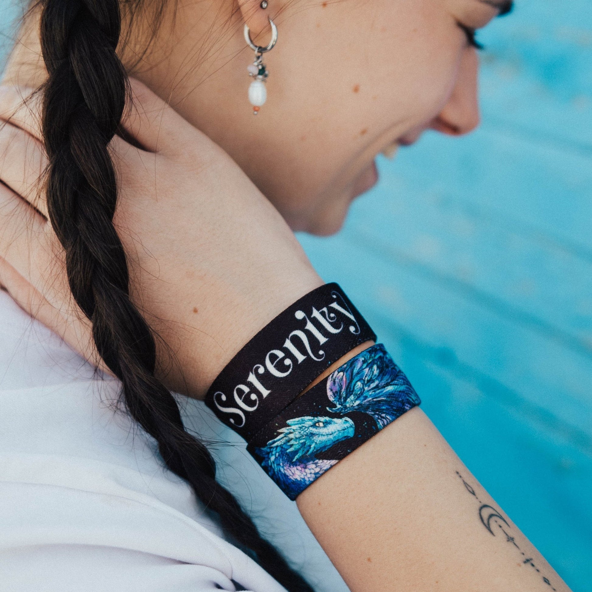 Person wearing a 'Serenity' wristband with a tattoo by a pool