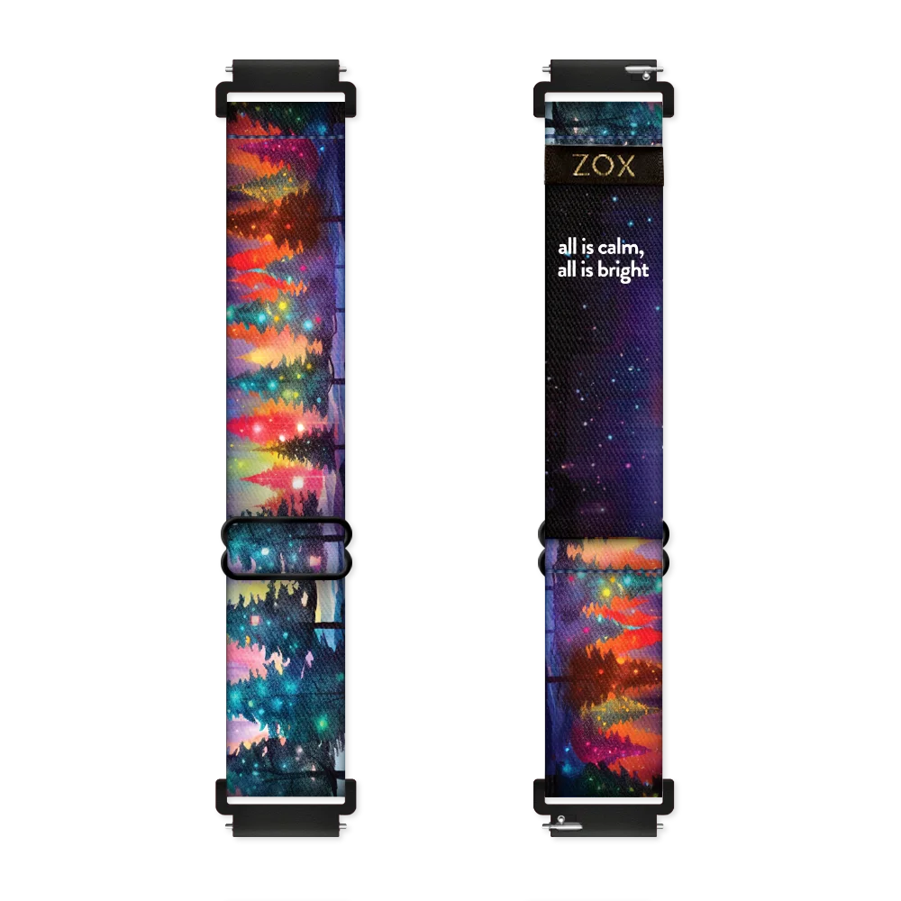 Android Watchband render of the All is Calm, All is Bright design, showing both the outside (left) and inside (right) of the band. The outer side on the left features a colorful, night-time landscape with a forest of evergreen trees illuminated by glowing lights in hues of red, green, and yellow. The inside on the right is black with the phrase 'all is calm, all is bright' printed in white text. The ZOX logo is on a black tag sewn near the top.