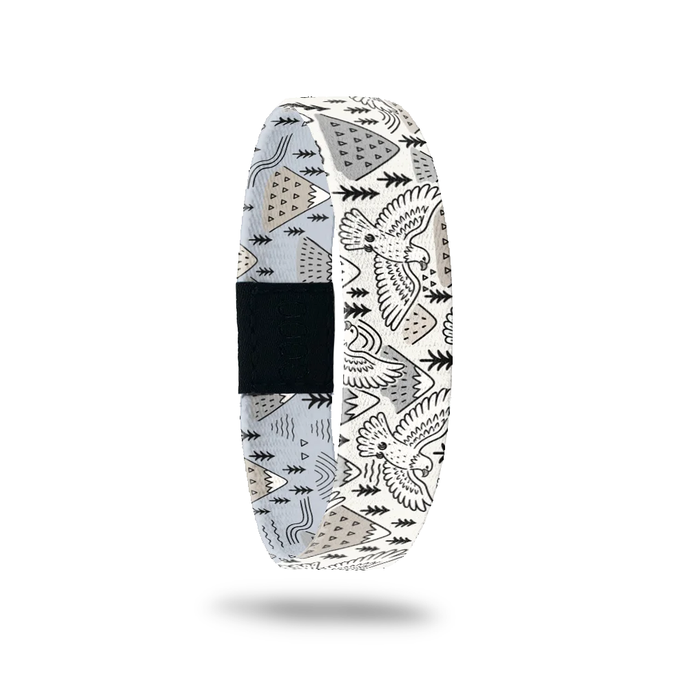 Above the Noise bracelet showing black and white mountains, pine trees and birds in flight