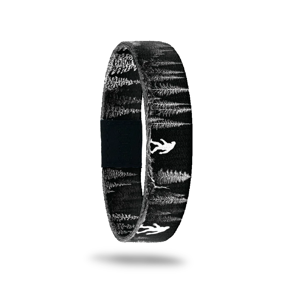 Believe bracelet showing a black and white pine forest with a pale sasquatch figure among the trees