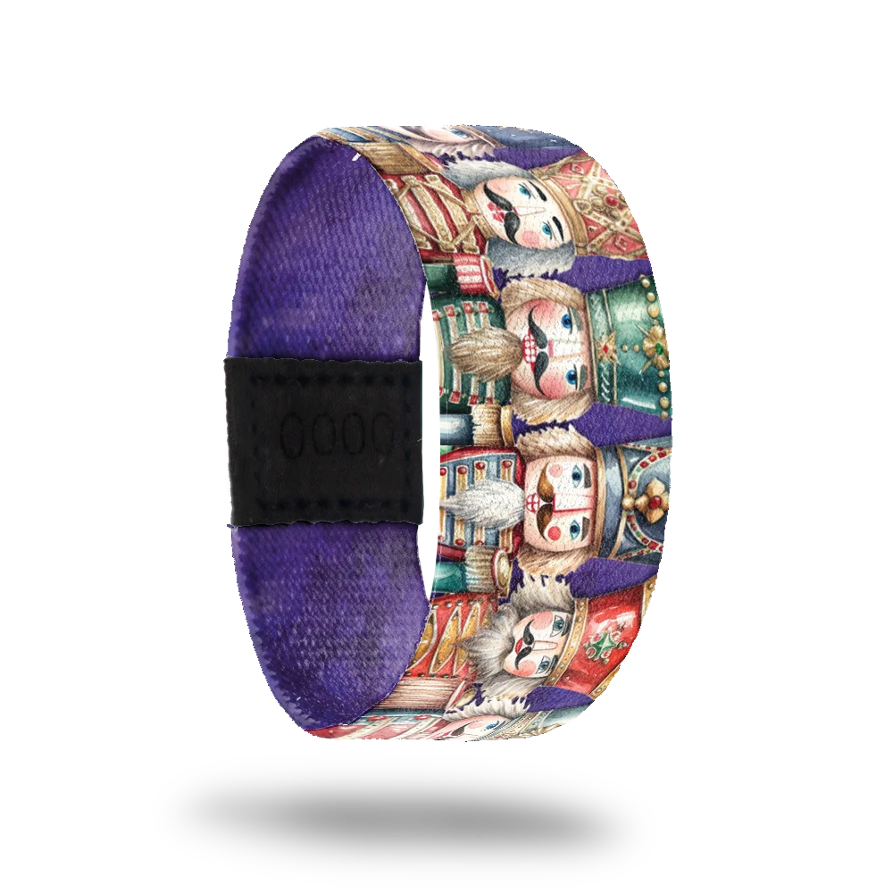 Purple strap with nutcrackers of varying shapes and sizes lines up next to each other. Inside is solid purple and says Dance Of Dreams. 