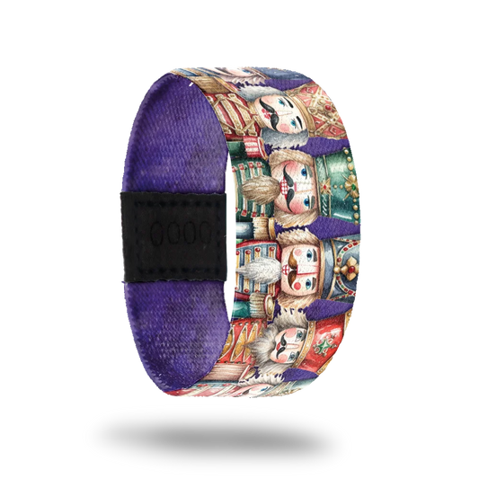 Purple strap with nutcrackers of varying shapes and sizes lines up next to each other. Inside is solid purple and says Dance Of Dreams. 