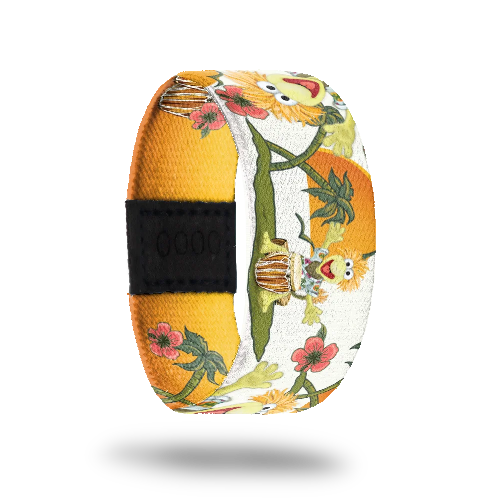 A colorful bracelet featuring Wembley from Fraggle Rock. Wembley is depicted joyfully playing a bongo drum, surrounded by a vibrant design of green vines and red flowers against a background of bright yellow and white. The artwork exudes a cheerful and tropical vibe.