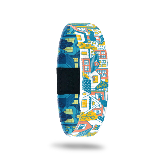 Wristband single with a design of a city block of houses and/or neighborhood. The colors are gold, light orange, blue and white. The inside is the same design but looks like nighttime so all of the houses are blue colored with glowing windows.The inside says Housing Is A Human Right. It comes with a matching charm. 