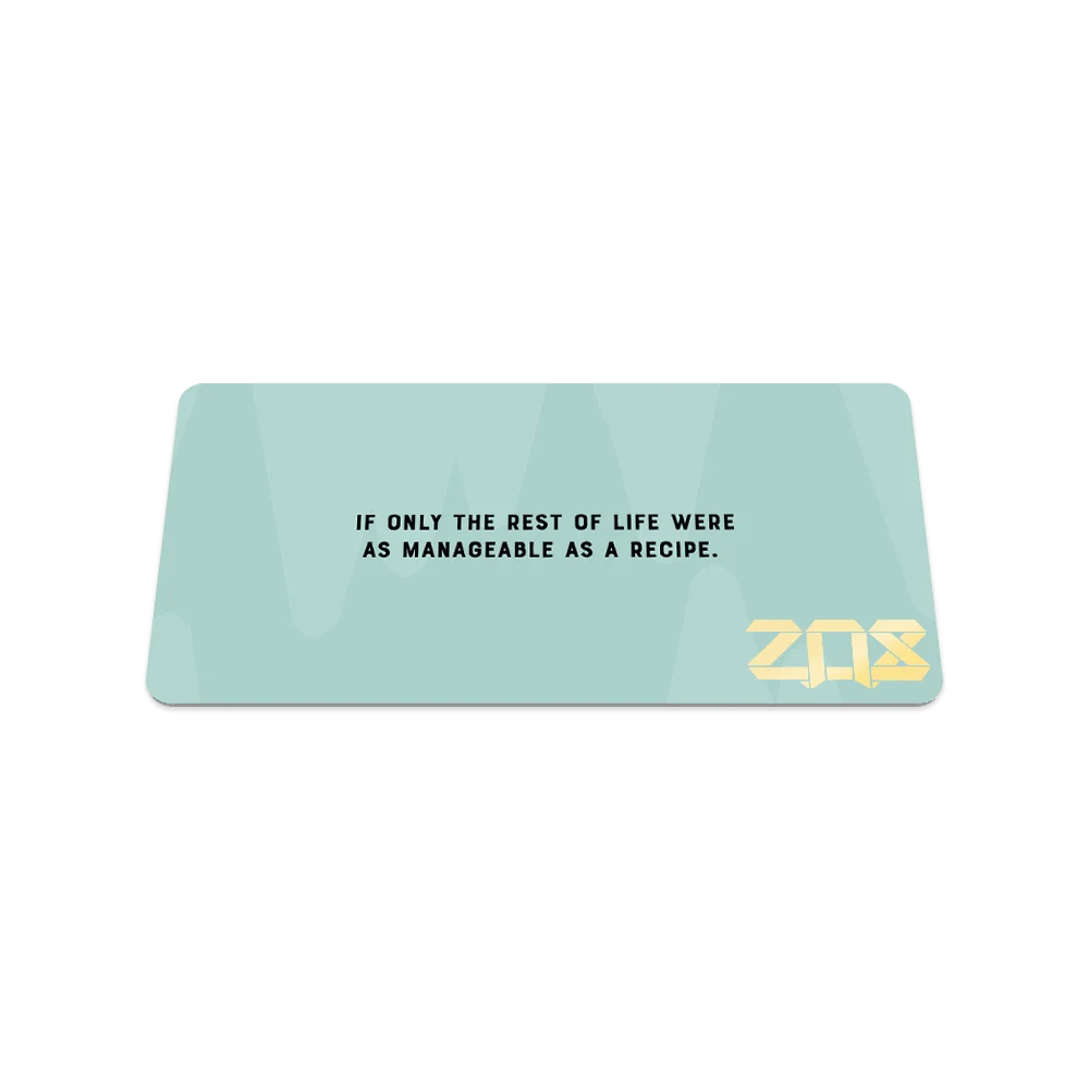 A rectangular bracelet display card with a pastel blue background and subtle abstract shapes. The text reads, "If only the rest of life were as manageable as a recipe," in black font, centered on the card. The ZOX logo is featured in bold gold lettering in the lower right corner.