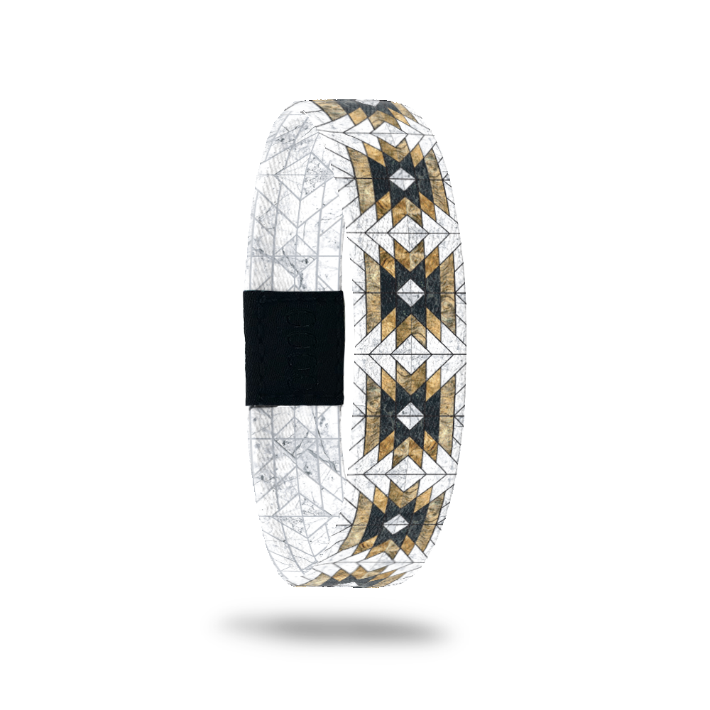 Single wristband with a white base. It has black and gold tribal, geometric designs all over. The inside is the same and says Love Who You Are. 