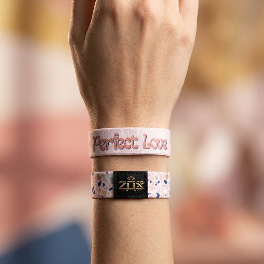 Hand wearing a wristband with 'Perfect Love' text against a blurred background