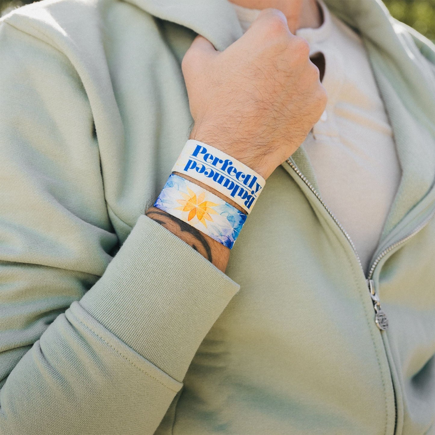 A close-up of the man’s wrist wearing the "Perfectly Balanced" bracelet. The design includes a soft, watercolor-style mandala with bold blue text reading "Perfectly Balanced" over the strap.