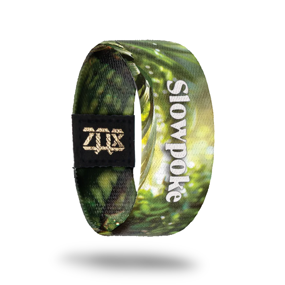 The inner side of the bracelet continues the green forest background with sunlight effects. White text reads "Slowpoke" along the strap. A black patch with a gold "ZOX" logo is also visible.