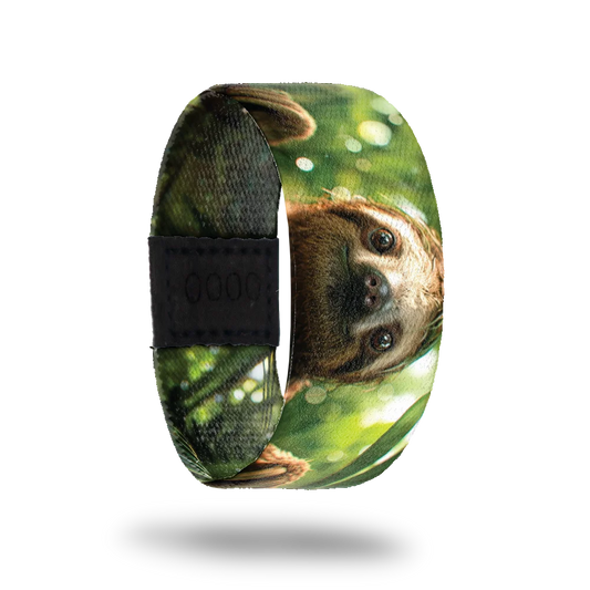 A bracelet featuring a close-up image of a smiling sloth's face set against a lush, green forest background with dappled sunlight filtering through the leaves. The sloth's expression is calm and content. A black rectangular patch with etched serial numbers is visible on one side of the strap.