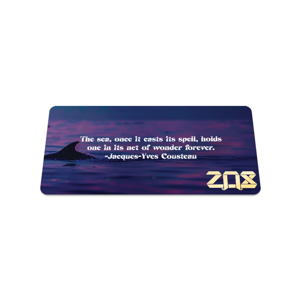 Product photo of the back of the Thalassophile collector's card, showcasing a close-up of a dolphin’s dorsal fin cutting through the tranquil water at sunset. White text in the center reads, "The sea, once it casts its spell, holds one in its net of wonder forever. – Jacques-Yves Cousteau." The gold "ZOX" logo is in the lower right corner.