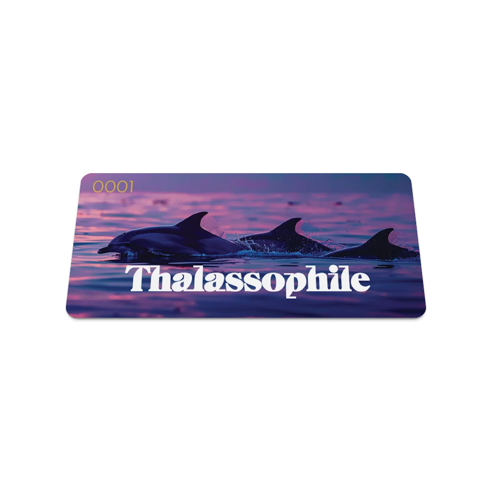 Product photo of the front of the Thalassophile collector's card, featuring a sunset ocean scene with silhouettes of three dolphins swimming in calm, purple-tinged waters. Bold white text across the bottom reads "Thalassophile," with the serial number "0001" in the top left corner.