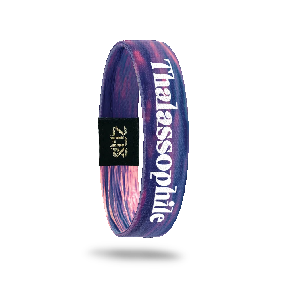 Product photo of the inside of the Thalassophile bracelet, featuring shades of a pink, purple, and orange sunset reflecting on the water. Bold white text reads "Thalassophile" vertically along the single. A black patch with a gold "ZOX" logo is also visible.