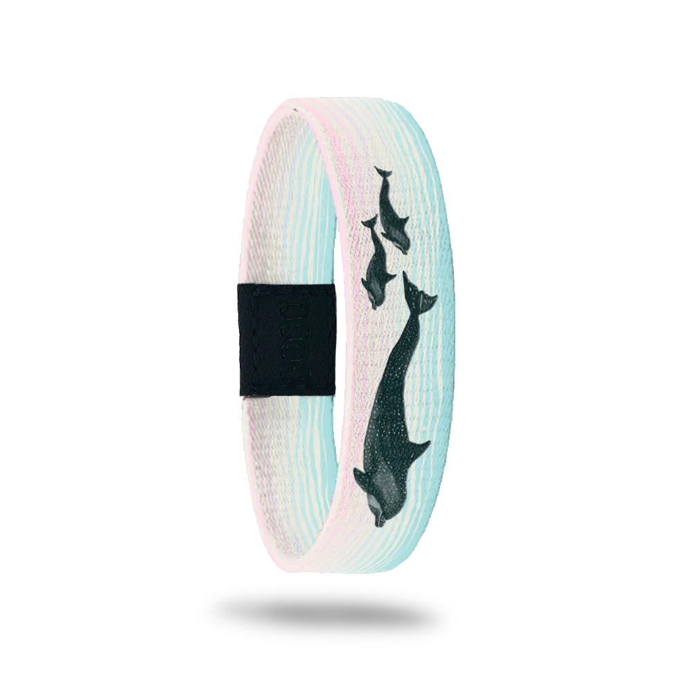 Product photo of the outside of the Waverider bracelet, featuring a pastel gradient background of light blue and soft pink. The design shows silhouettes of four dolphins gracefully swimming upward. A black rectangular patch with etched serial numbers is visible on one side of the single.