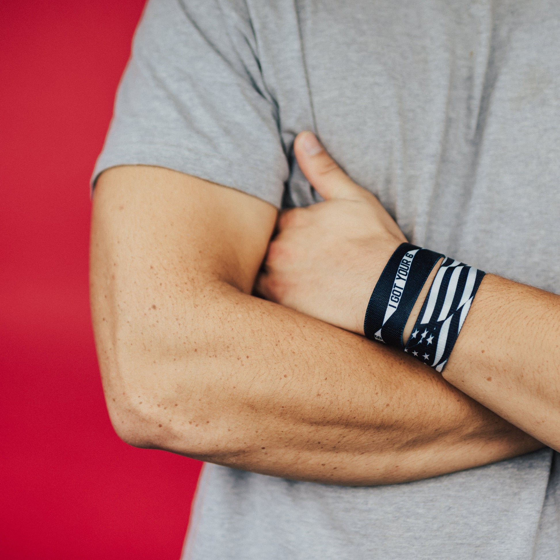 Studio image of model's arms crossed and close up of 2 I Got Your Six on their wrist