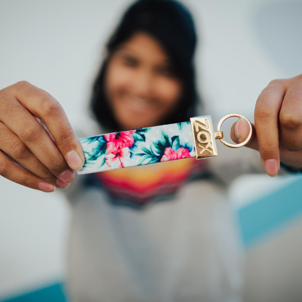 Model holding Gold ZOXLOX with green and pink floral strap attached.