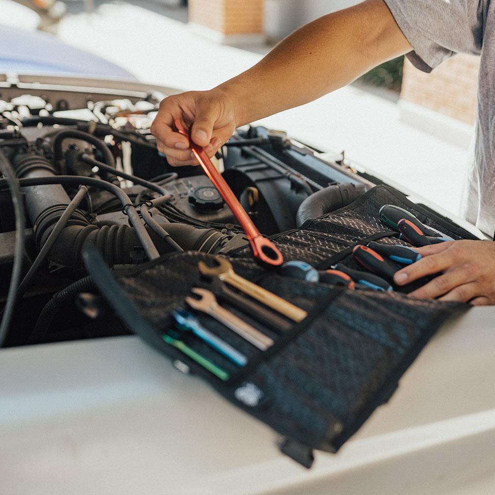 A man fixing his car with the roll opened up full of tools on the side of his truck