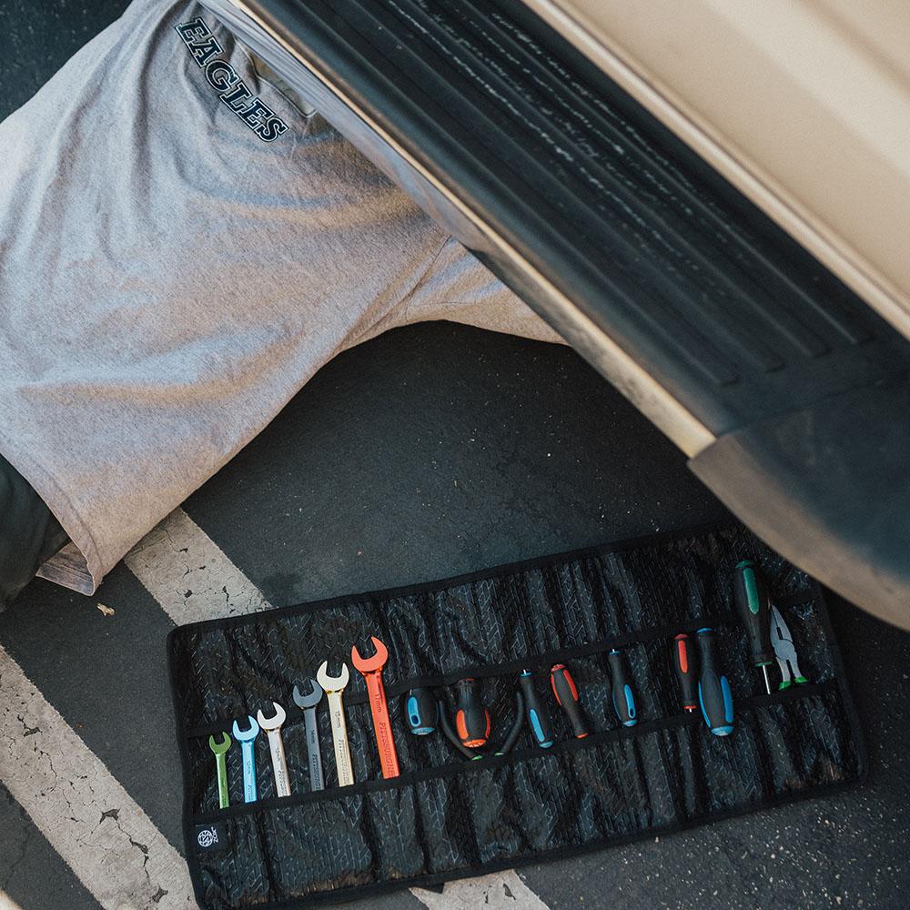 Man under his car with his tools next to him in the roll that is fully opened